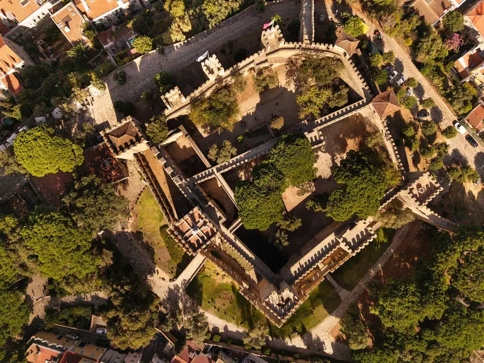 Vue aérienne du château de São Jorge : l'enceinte, ses tours et les jardins, entourés des toits du quartier